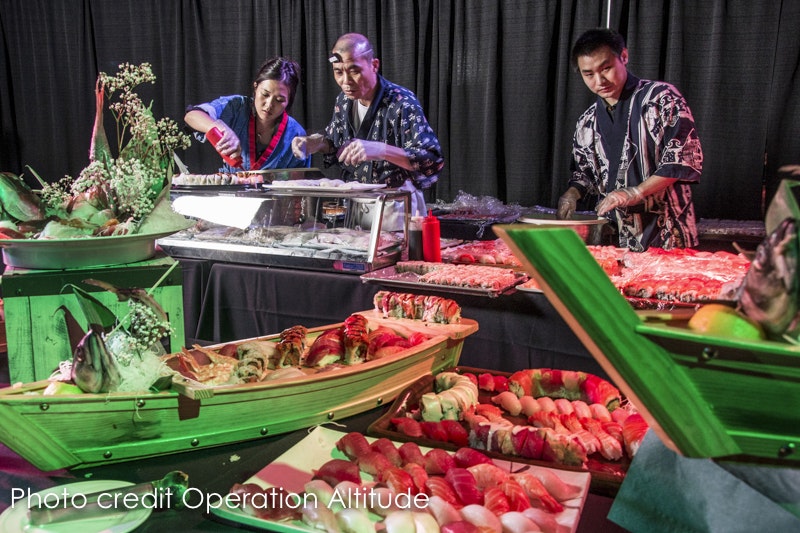 Sushi chefs preparing food at a buffet with a variety of sushi on display.