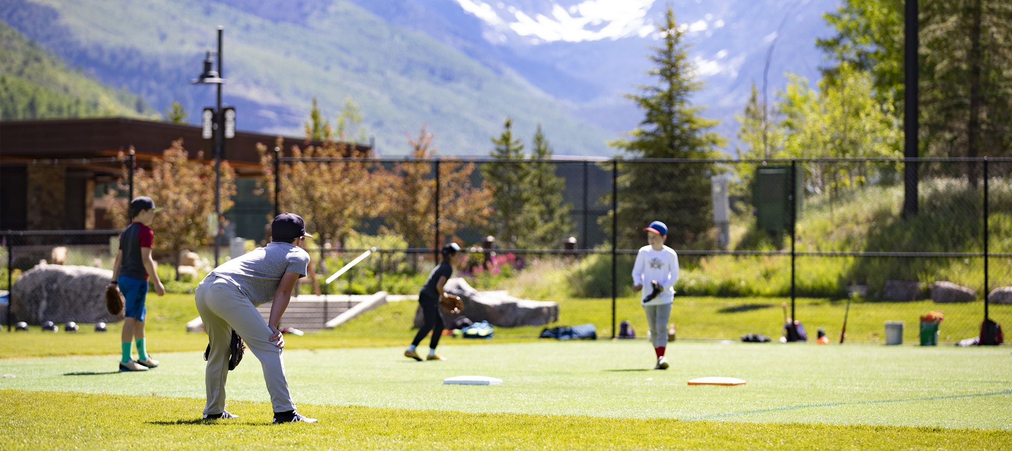 A baseball game in progress on a sunny field with mountains in the background.