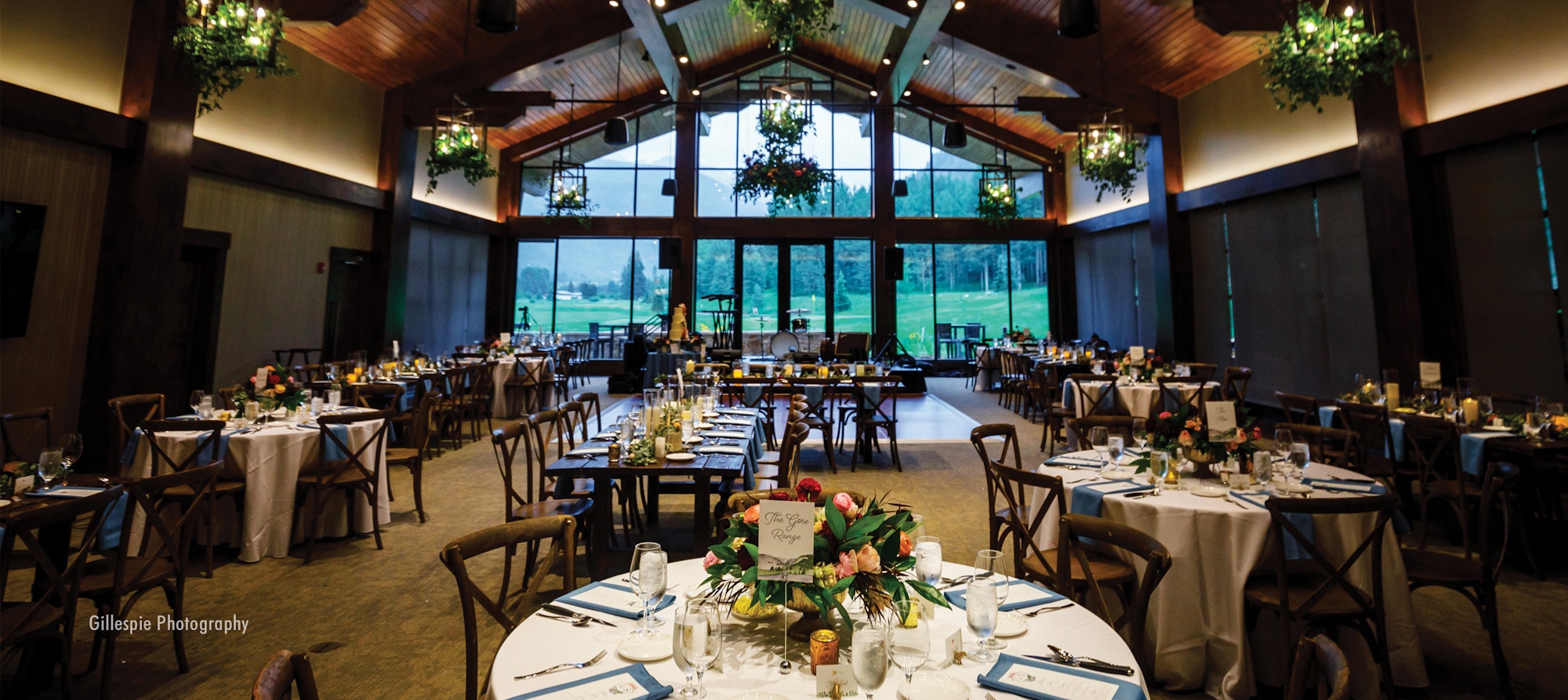 Elegant indoor event space with dining tables, floral centerpieces, and large windows offering a view of the green landscape outside.
