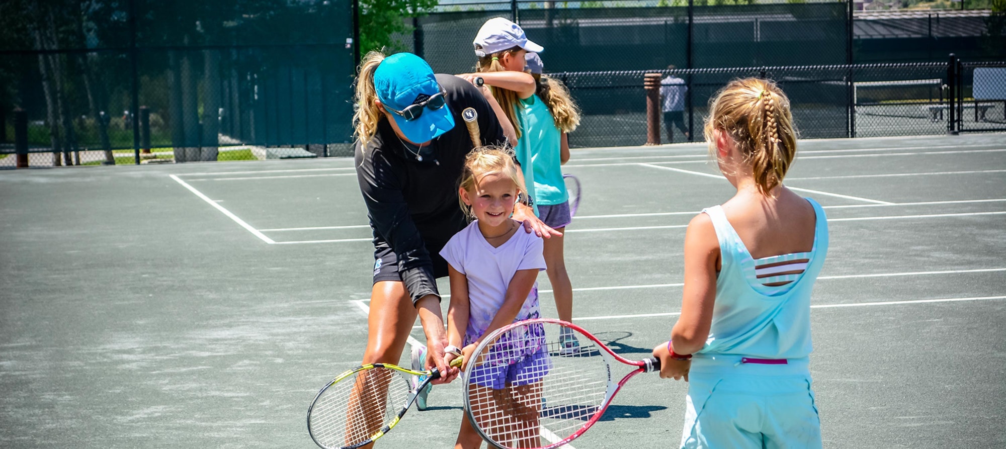 Tennis coach instructing young players on a sunny court.