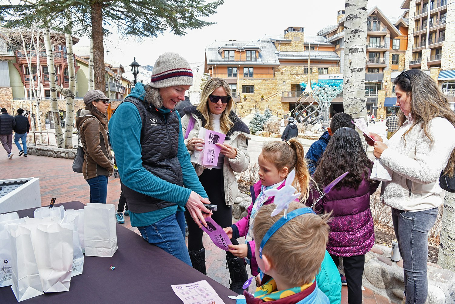 People at an outdoor event with a table, paper bags, and pamphlets.