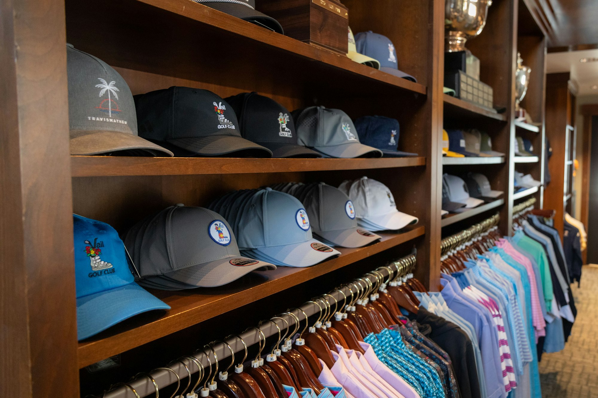A collection of caps and polo shirts on wooden shelves in a store.