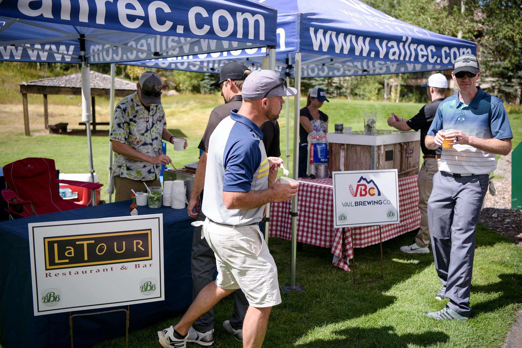 People at an outdoor event with tents, drinks, and signs for a restaurant and brewery.