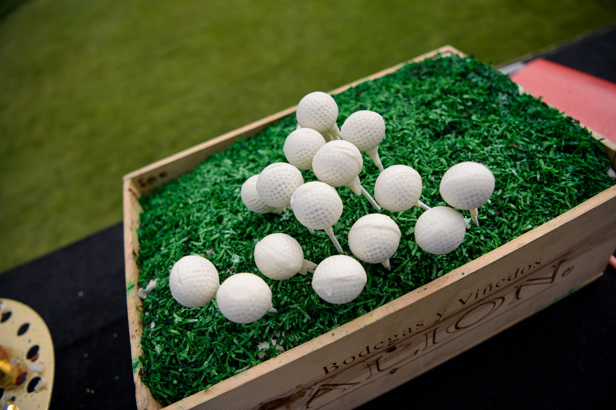 Golf balls on tee pegs inserted in a box with artificial grass.