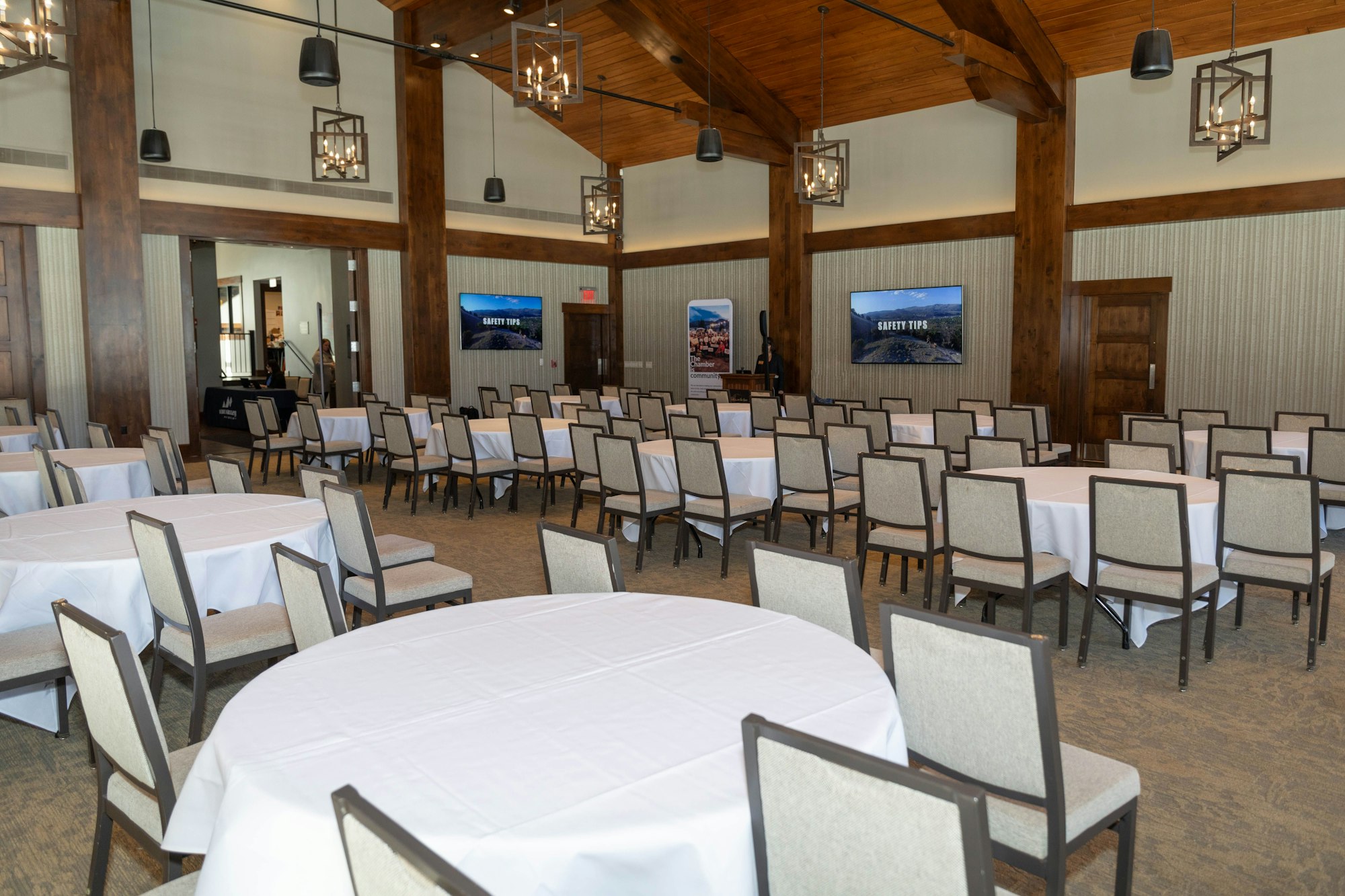 An empty conference room with round tables, chairs, and two TV screens displaying "Safety Tips".