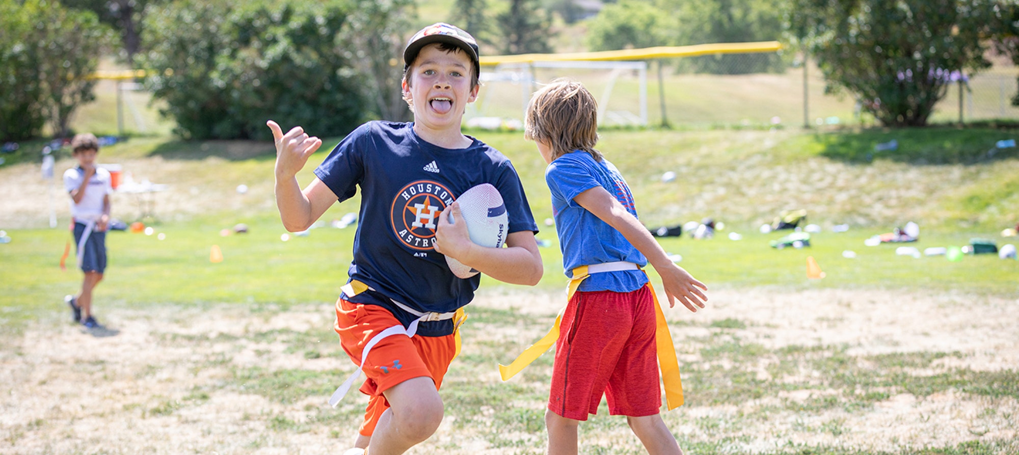 Kids playing flag football on a sunny day, one excitedly running with the ball.