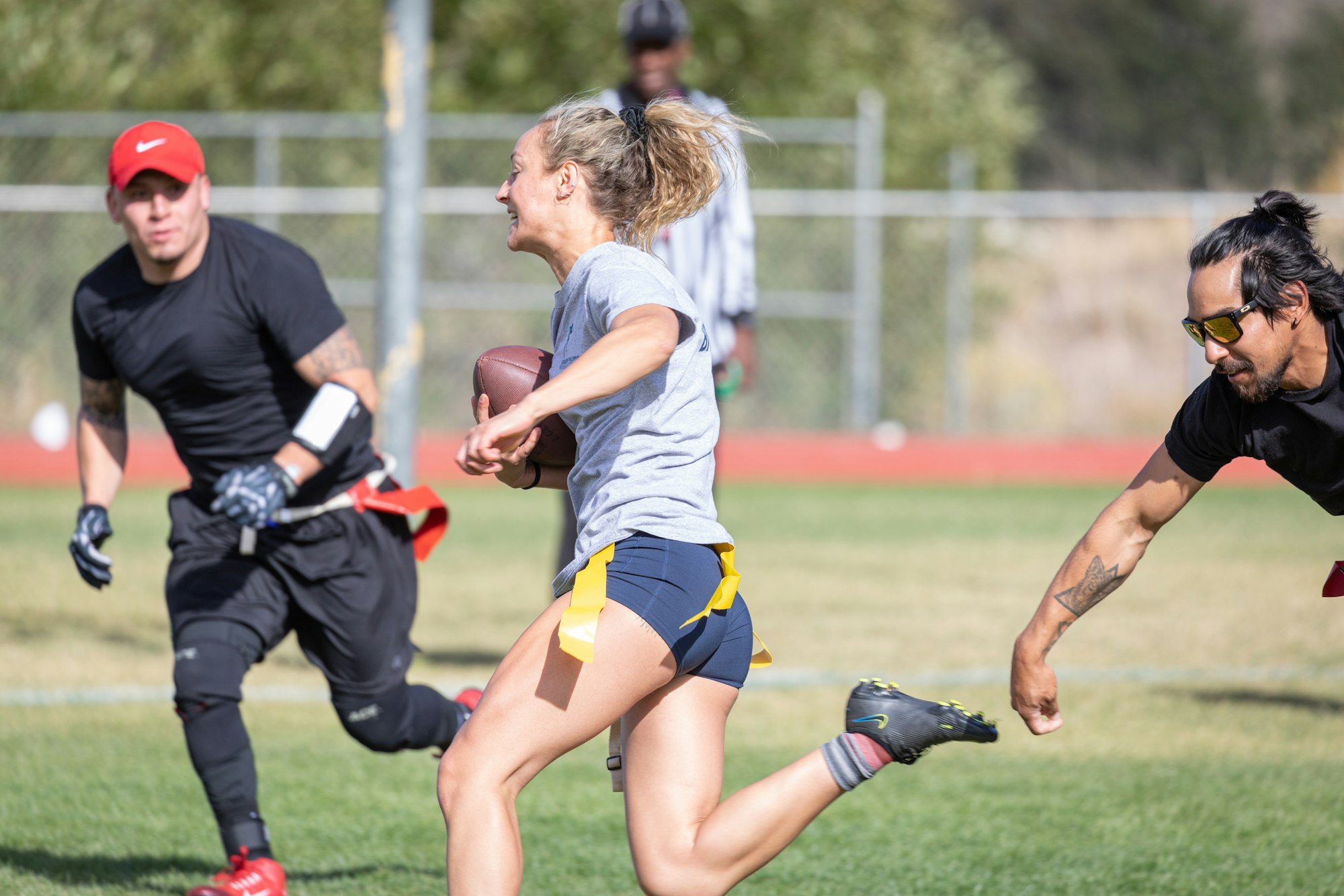 People playing flag football, woman running with ball, two men attempting to grab her flag.