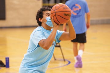 Person wearing a mask about to shoot a basketball in an indoor gym.