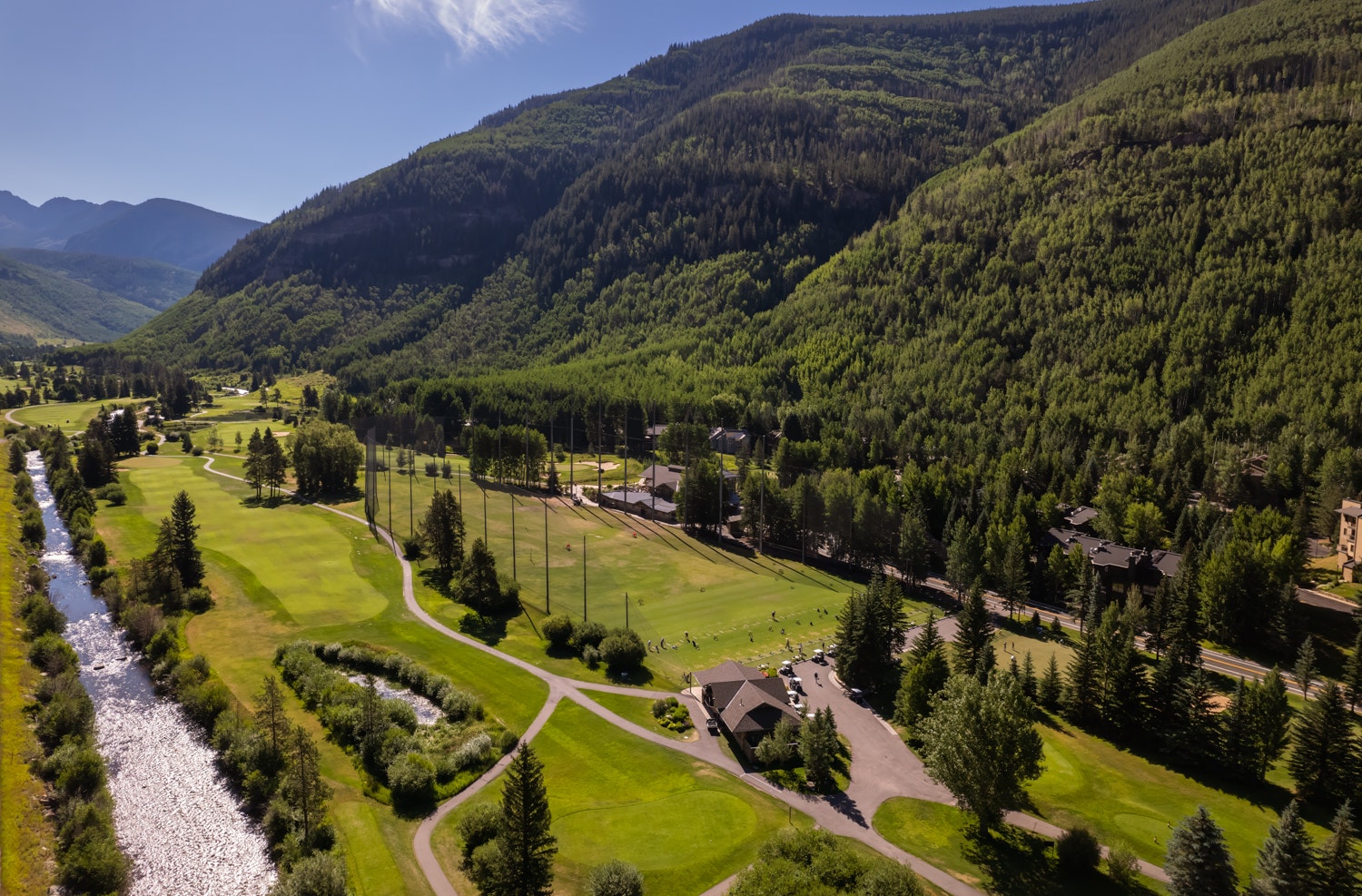 Aerial view of the Vail Golf Club course, surrounded by forested hills under a blue sky.