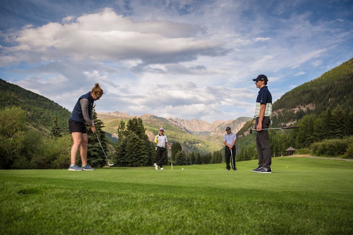 Four golfers on a green with mountains in the background.