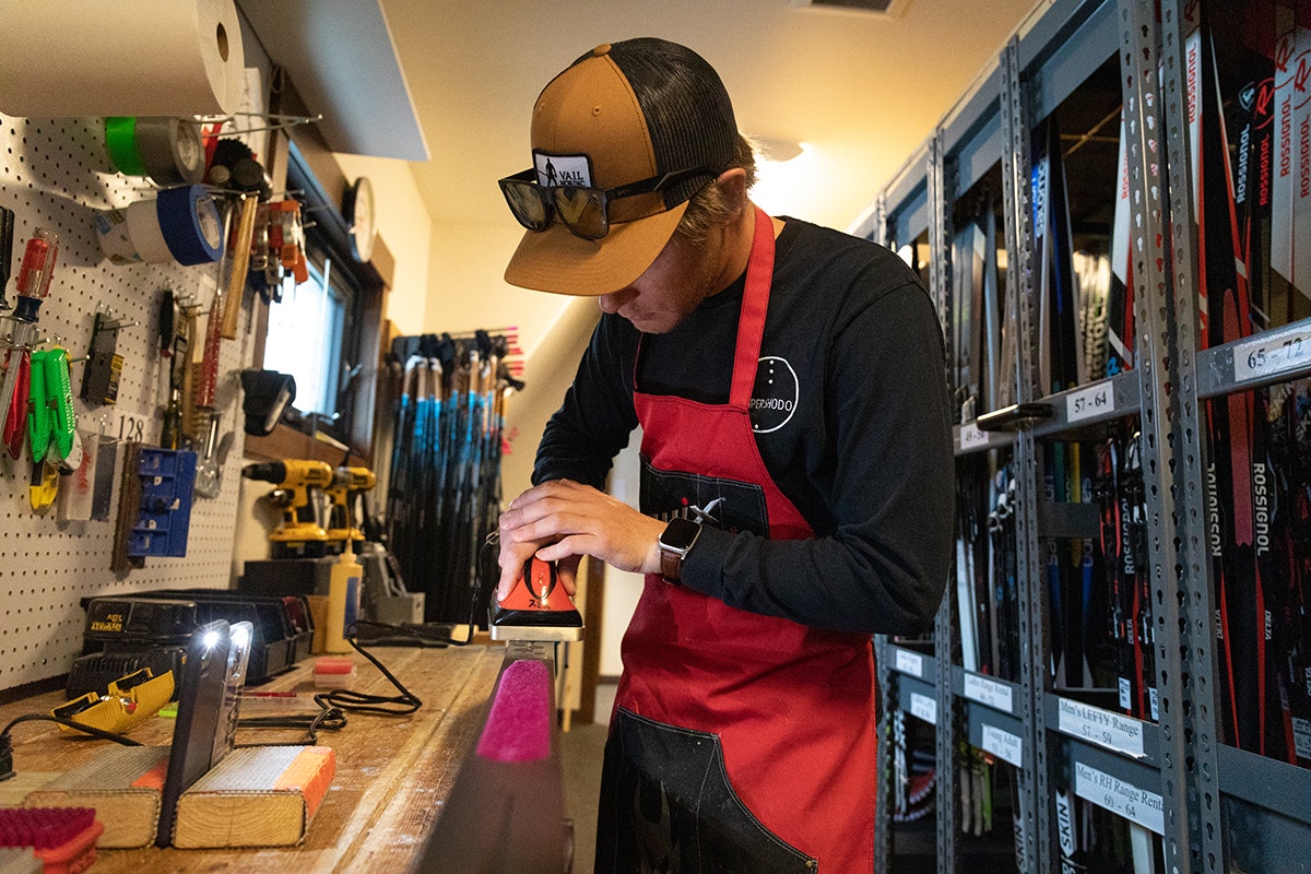 A person tuning skis in a workshop filled with equipment.