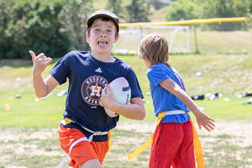 Two kids playing frisbee in a park, one cheering and holding the frisbee, sports field in background.