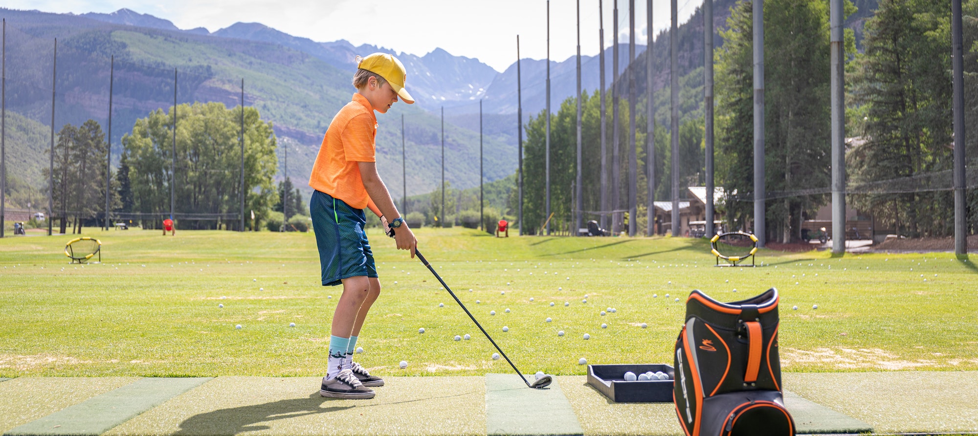 A boy playing golf at a driving range with mountains in the background.
