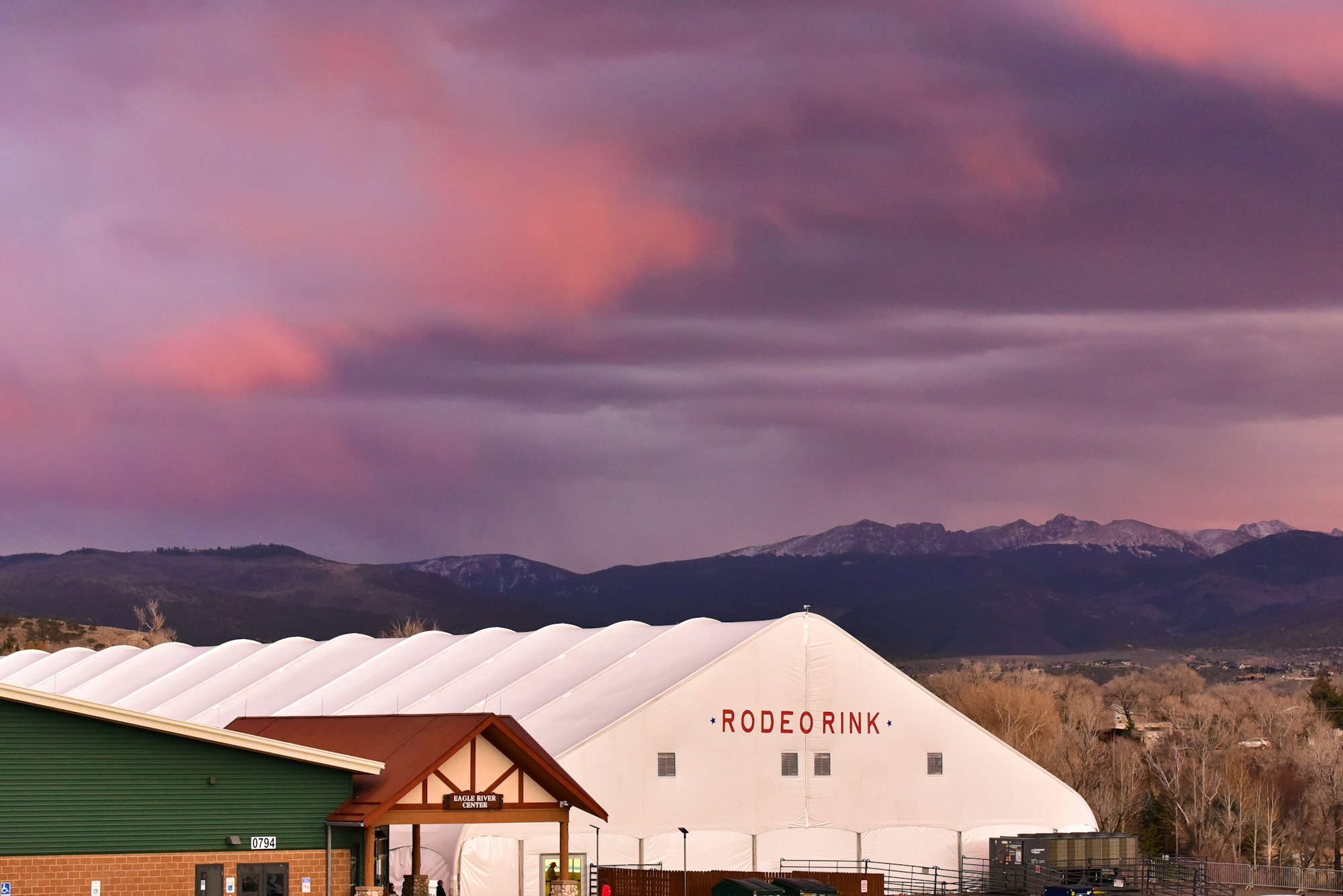 A colorful sunset over a snowy mountain backdrop featuring a building labeled "Rodeo Rink" and "Eagle River Center."