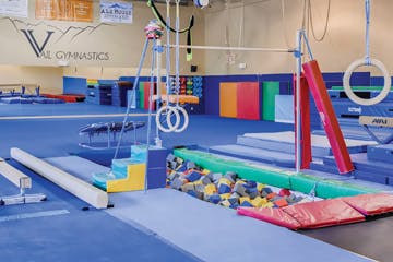 Gymnastics gym with various equipment like rings, beams, bars, and foam pit.