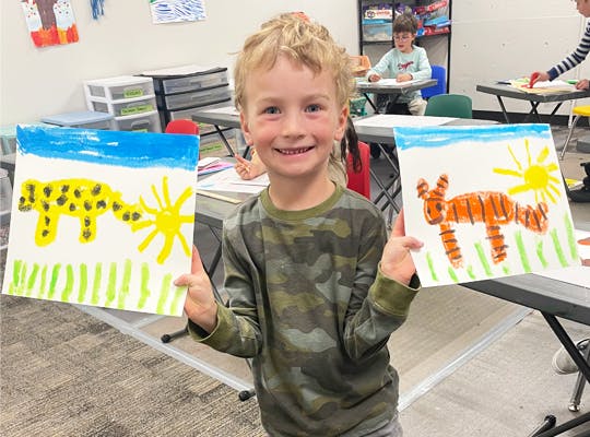 A happy child showing off two colorful animal paintings.