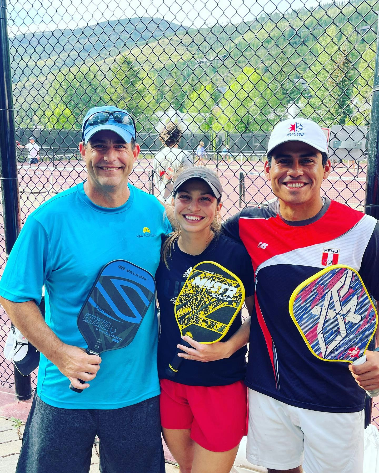 Three people holding paddleball racquets, smiling, on a court.