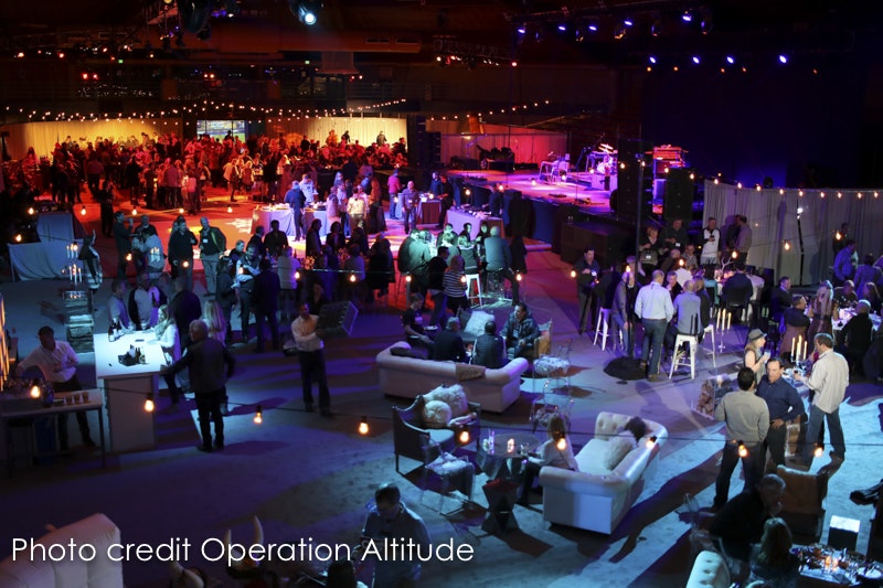 Indoor event with people mingling, stage set up, lounging areas, and mood lighting.