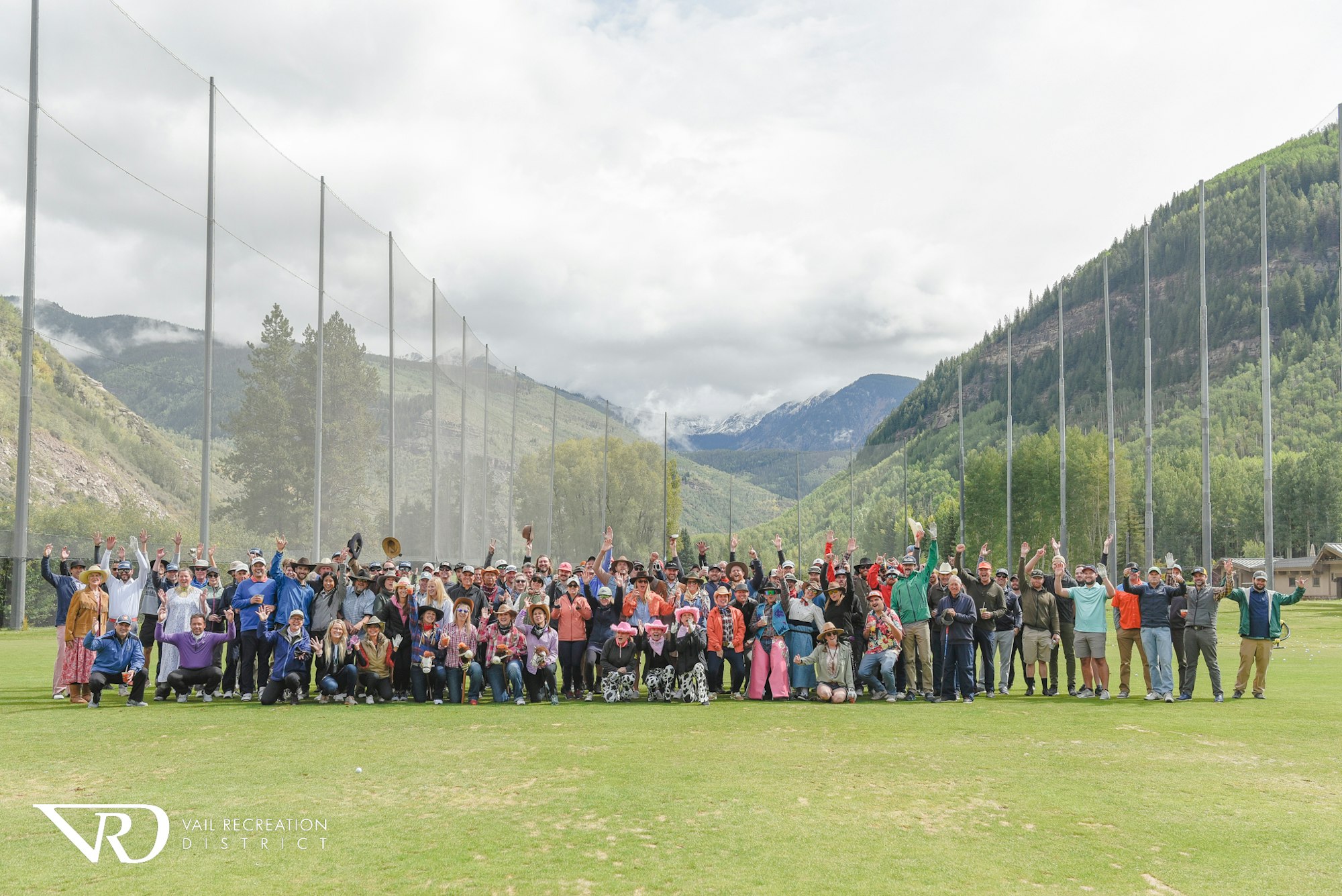 Group of people posing cheerfully on a sports field with mountains in the background.