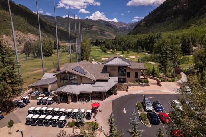 Golf club with parked carts, surrounded by mountains and greenery under a partly cloudy sky.