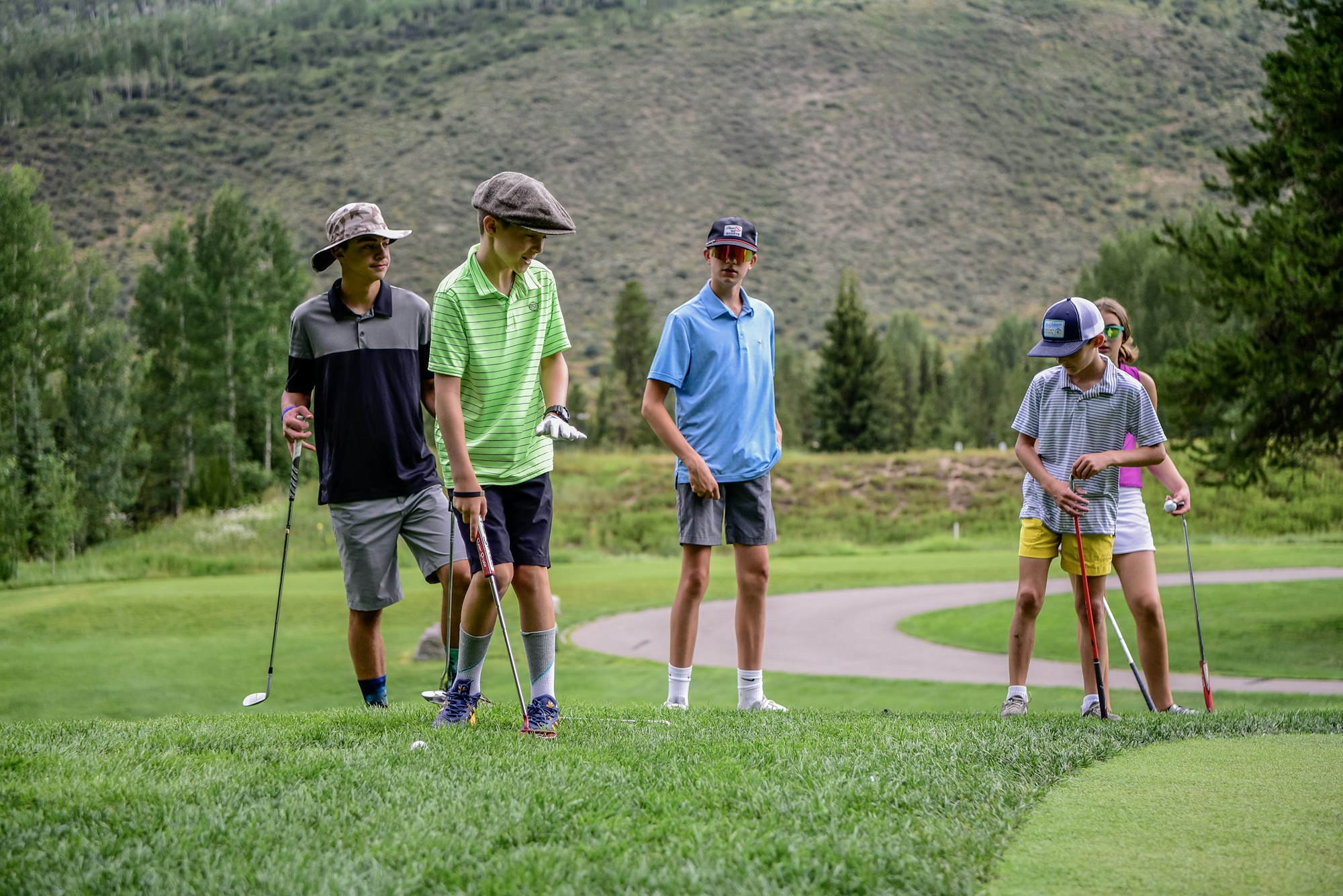 A group of young golfers on a green course with clubs, preparing to play.