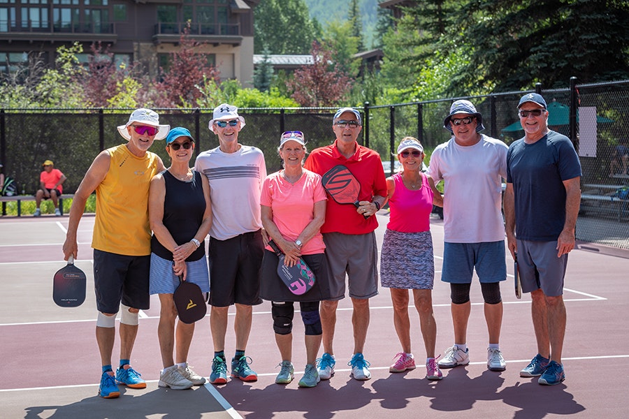 A group of people smiling on a tennis court, holding pickleball paddles.