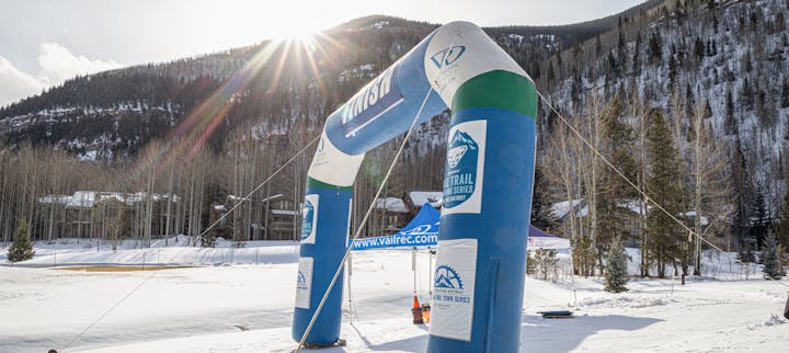 Inflatable arch at a snowy mountain base with sun glare.