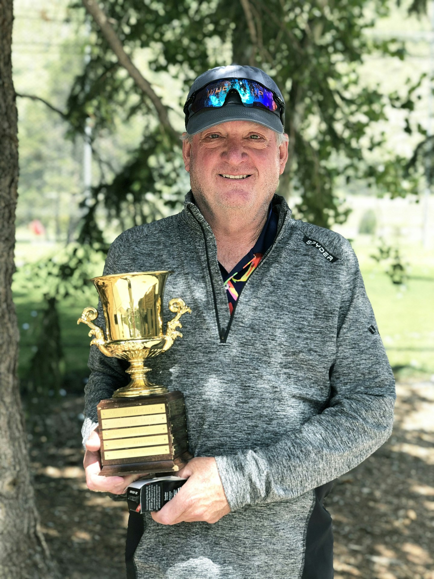 A smiling person holding a large trophy outdoors.