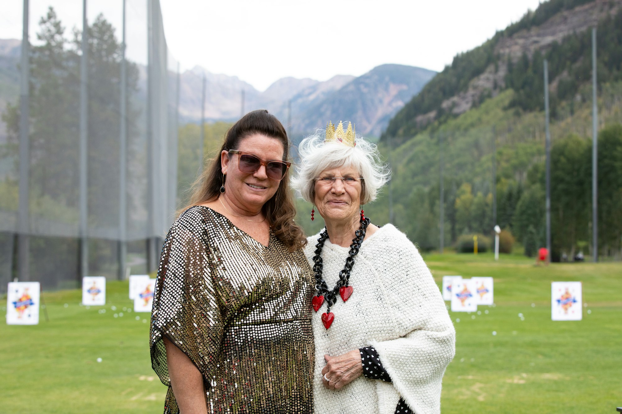 Two women posing together in front of a golf course with mountain scenery in the background.