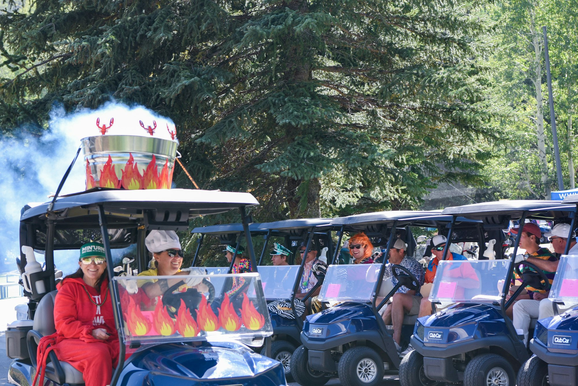 People in themed golf carts, with flames and lobsters decoration, in a parade-like setting surrounded by trees.