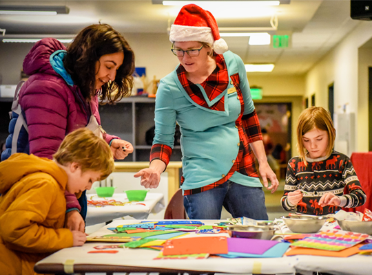 People making crafts, a woman in a Santa hat, festive atmosphere.