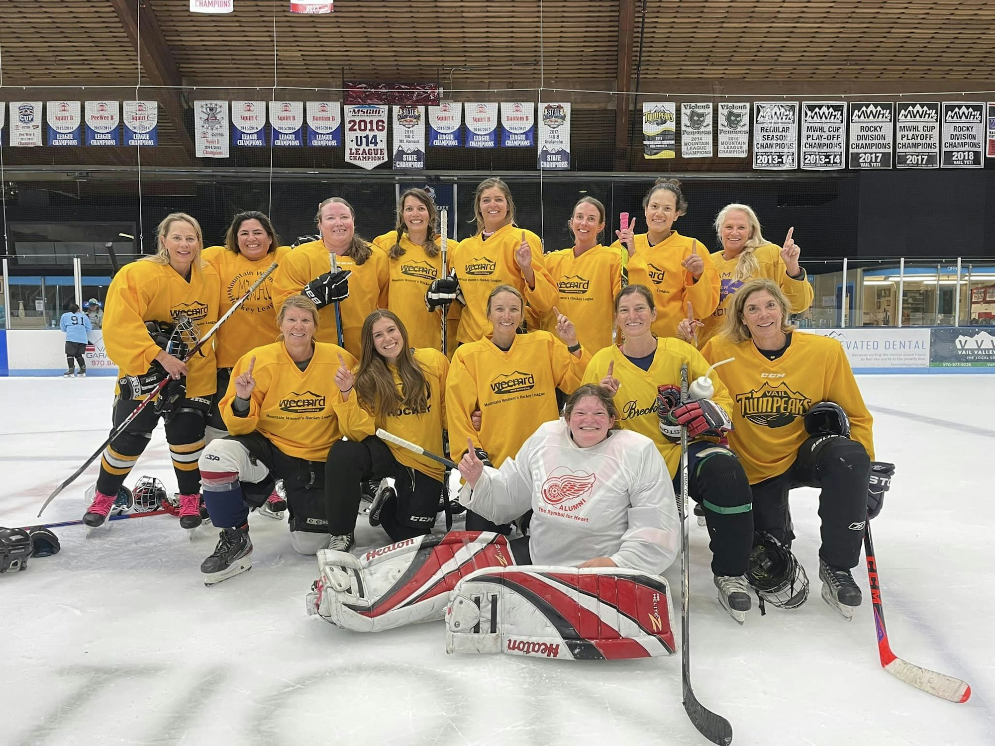 A happy women's hockey team posing on the ice in yellow jerseys.