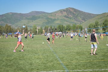 Outdoor scene with people playing soccer, mountains in the background, on a sunny day.