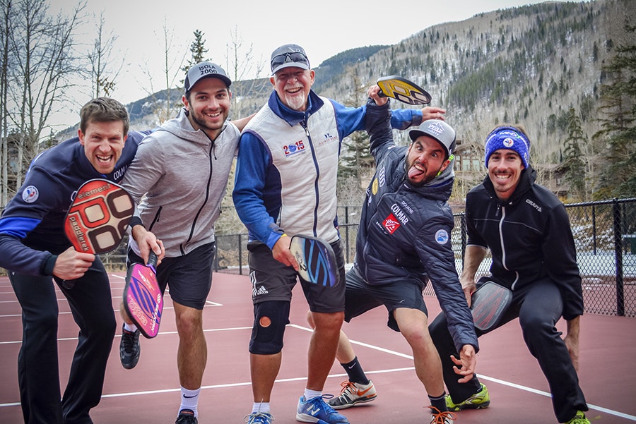 Five people posing with paddleball equipment on a court, mountains in the background.