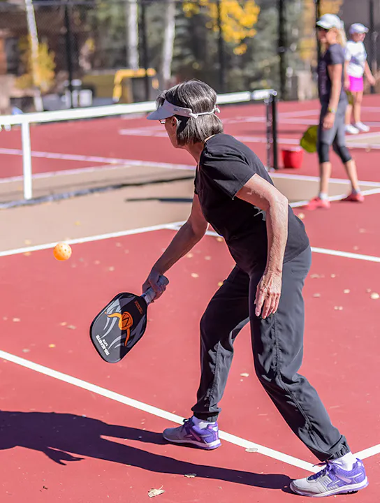 Person plays pickleball on a red court, ready to hit a yellow ball with a paddle.