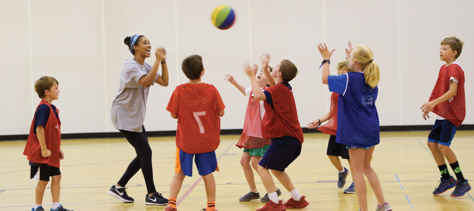 Coach surrounded by smiling kids reaching for basketball as it is thrown in the air