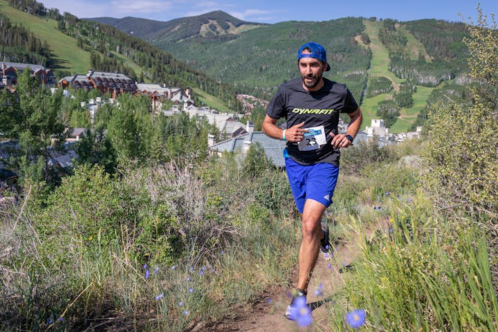 A runner with a bib number in a scenic mountain trail race near a resort.