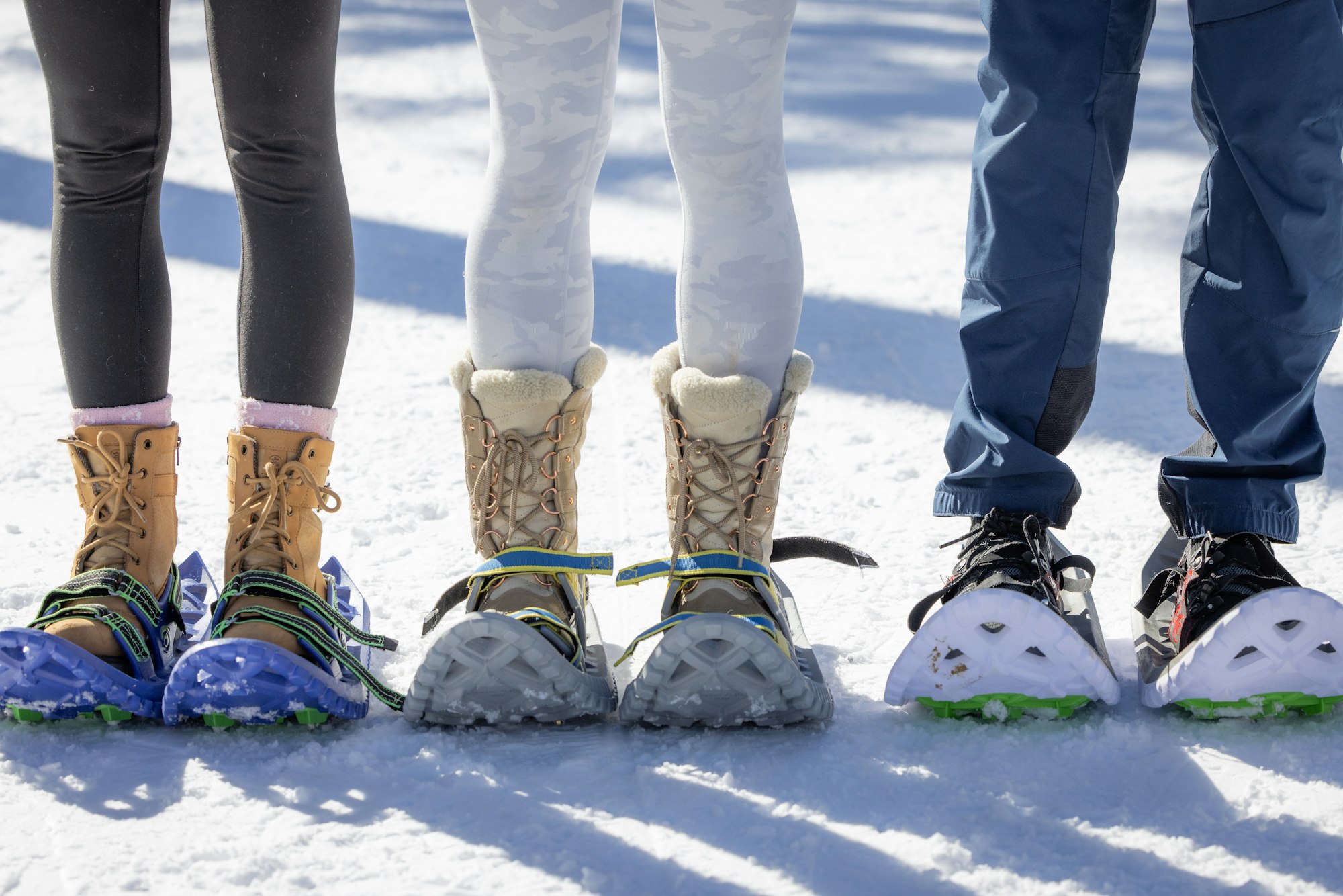 Three people wearing snowshoes and winter boots standing on snow.