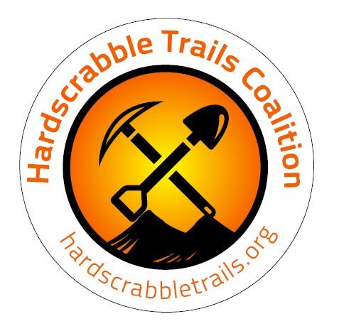 A logo for Hardscrabble Trails Coalition featuring a pickaxe and shovel crossed over a mountain silhouette inside an orange circle.