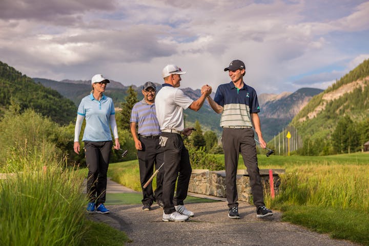 Four golfers are fist bumping on a course with mountains in the background.
