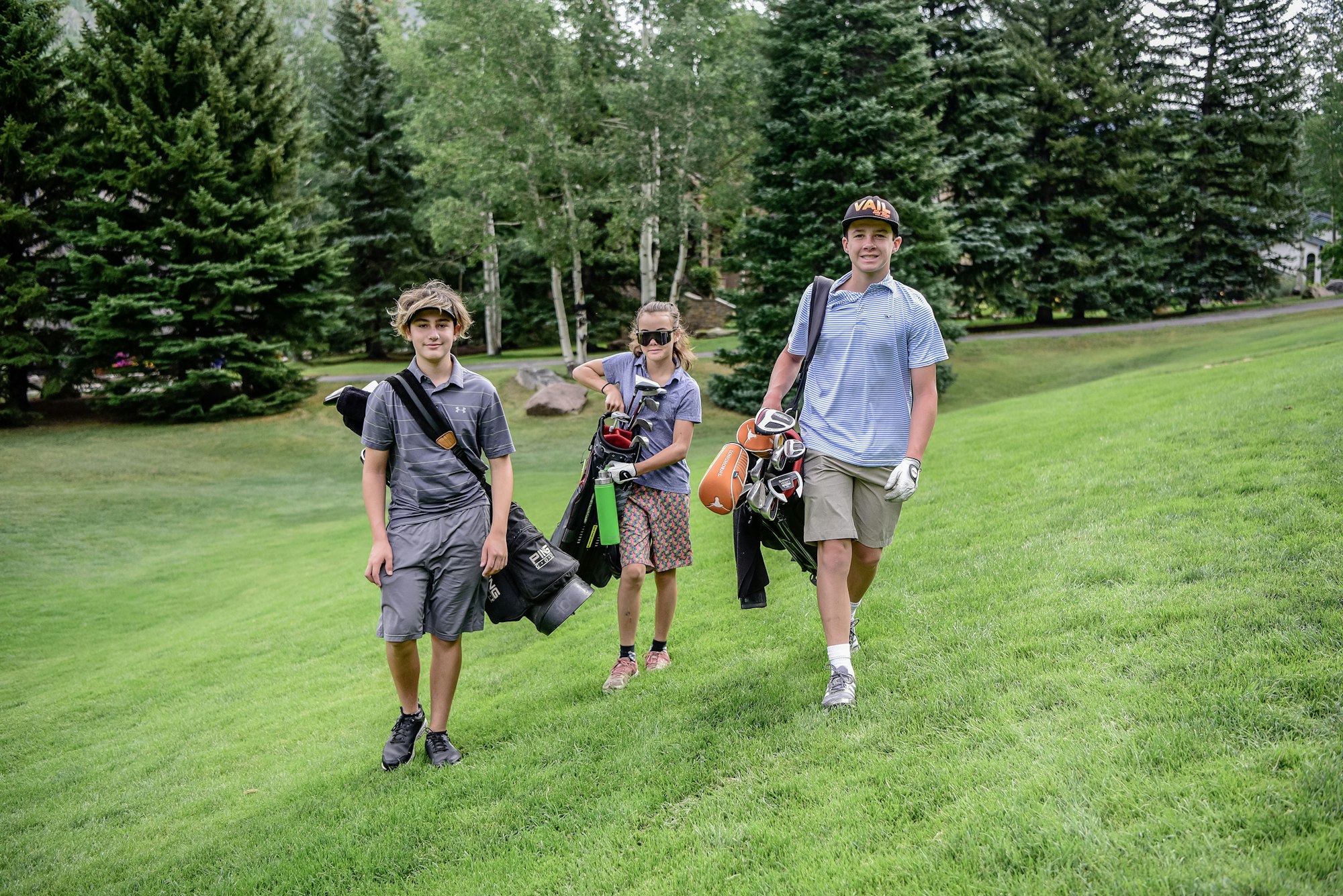 Three young golfers with clubs strolling on a lush green course.