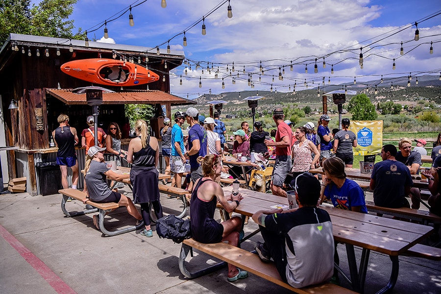People socializing at an outdoor patio with string lights and a kayak mounted on the wall.