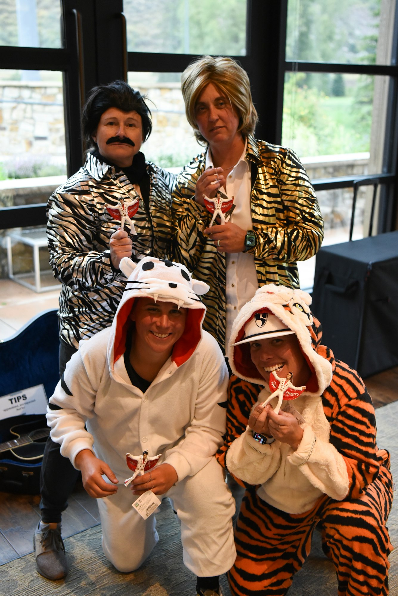 Four people in costumes holding miniature guitars, two dressed as animals, and two with zebra-striped jackets. They're smiling indoors.