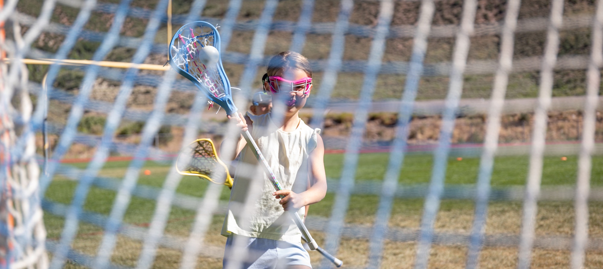A child wearing protective eyewear playing lacrosse behind a goal net.