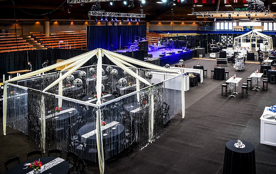 An event setup with a stage, tables, chairs, and a draped canopy structure.