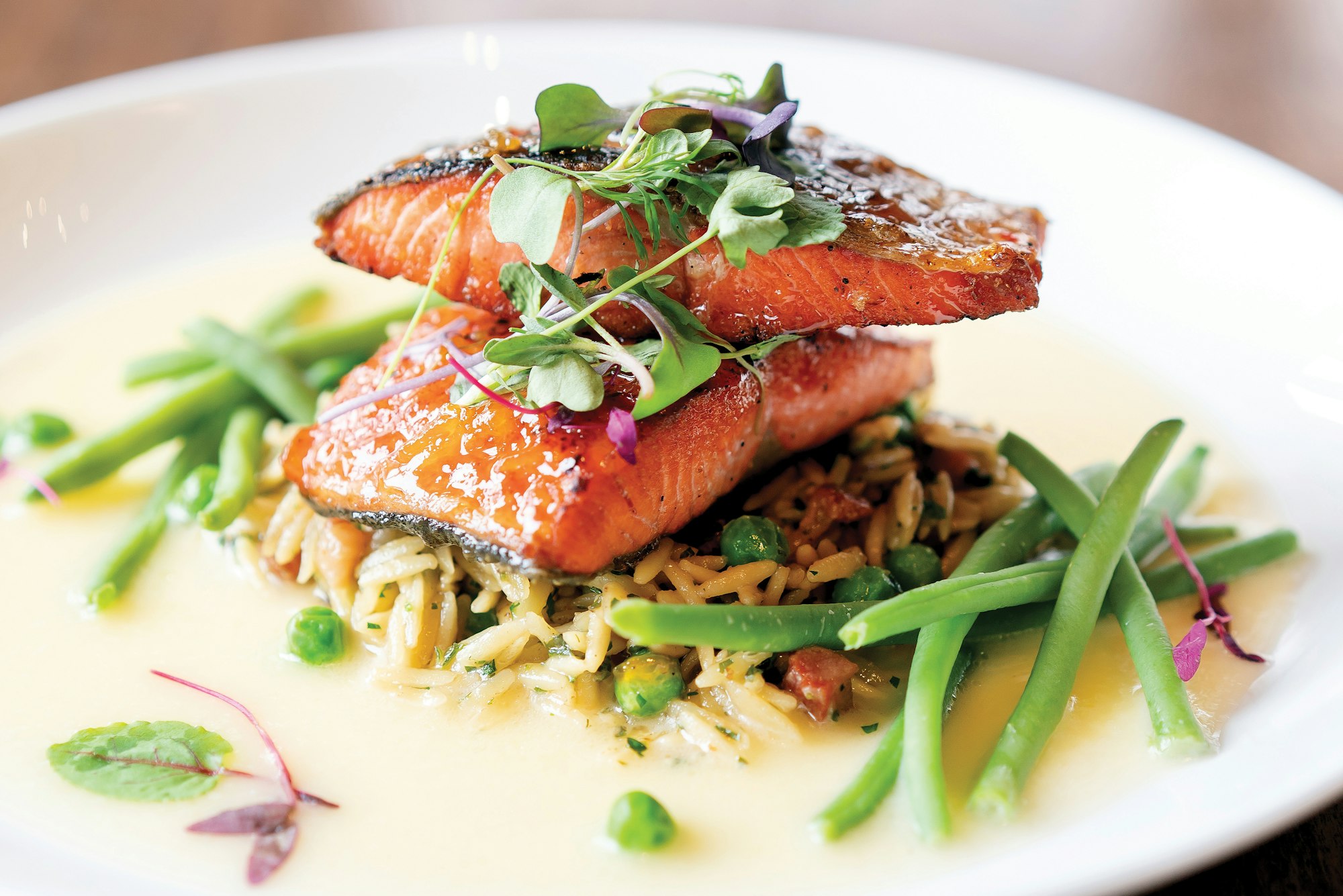 Grilled salmon on a bed of rice with peas and green beans, garnished with microgreens.