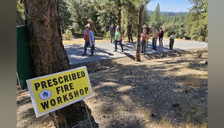 People attending a "Prescribed Fire Workshop" outdoors, with informative sign in the foreground.