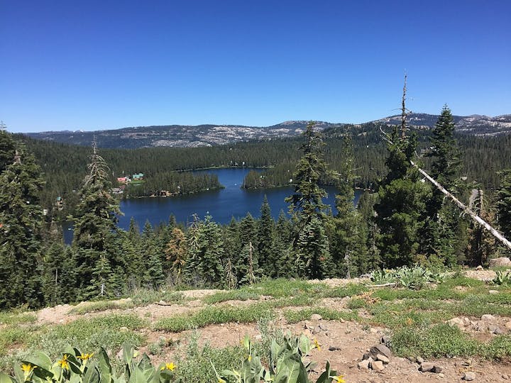 A serene lake surrounded by dense forests, rolling hills, and clear blue skies.