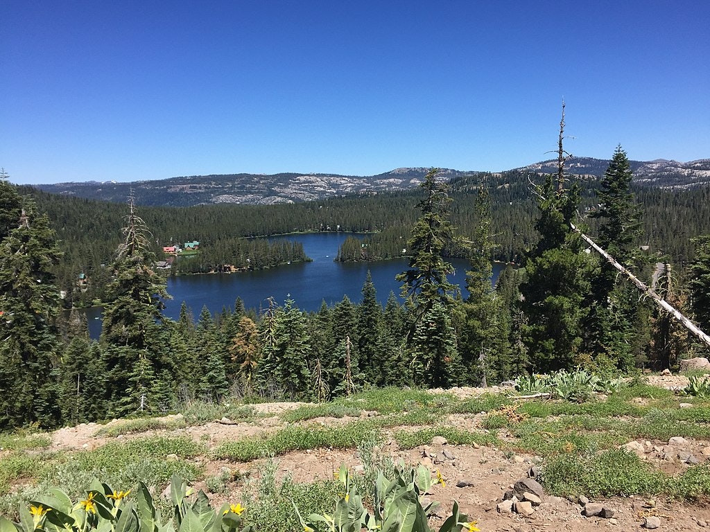 A serene lake surrounded by dense forests, rolling hills, and clear blue skies.