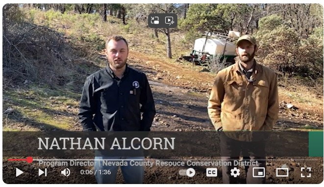 Two men stand outdoors on a dirt path next to trees and equipment, with a name overlay showing "Nathan Alcorn."